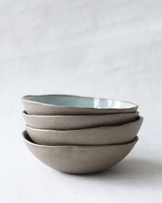 A set of handmade ceramic bowls in gray color, stacked on top of each other on a light background.