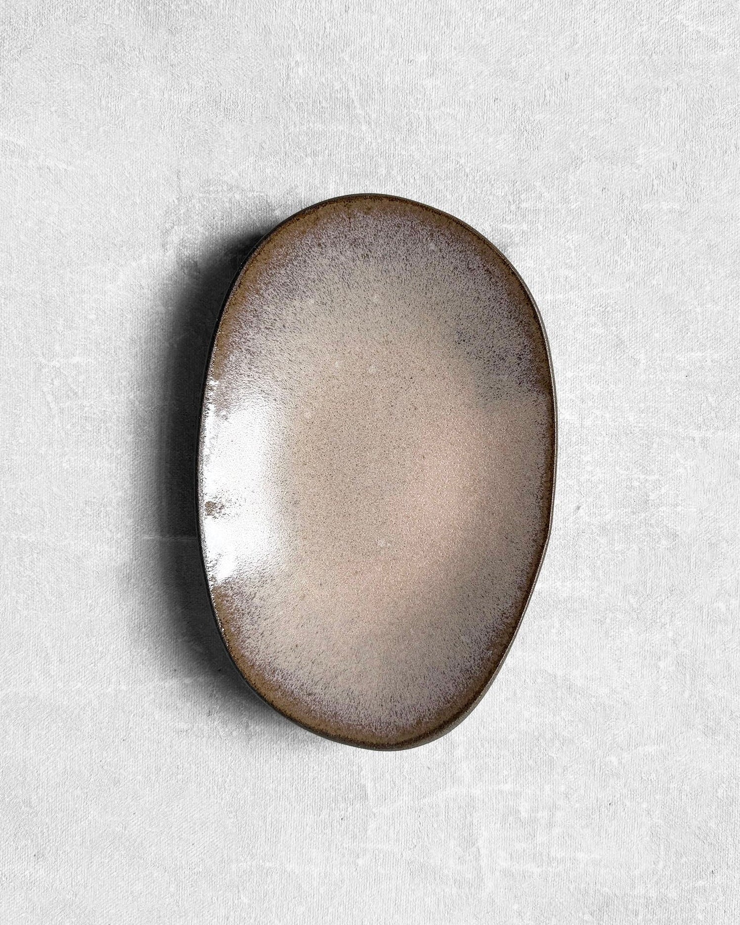 Oval ceramic plate with a gradient finish on a textured white background